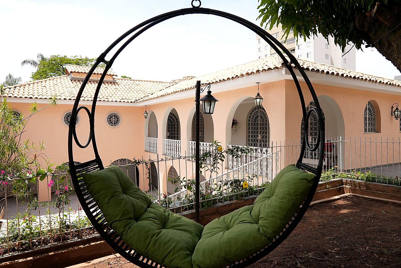 Balanço suspenso sob a mangueira, com a casa colonial e suas janelas em arco ao fundo