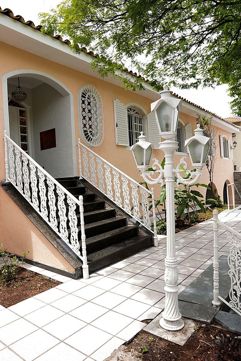 Escadaria de entrada com guarda-corpo branco e poste colonial do Casarão José Morada