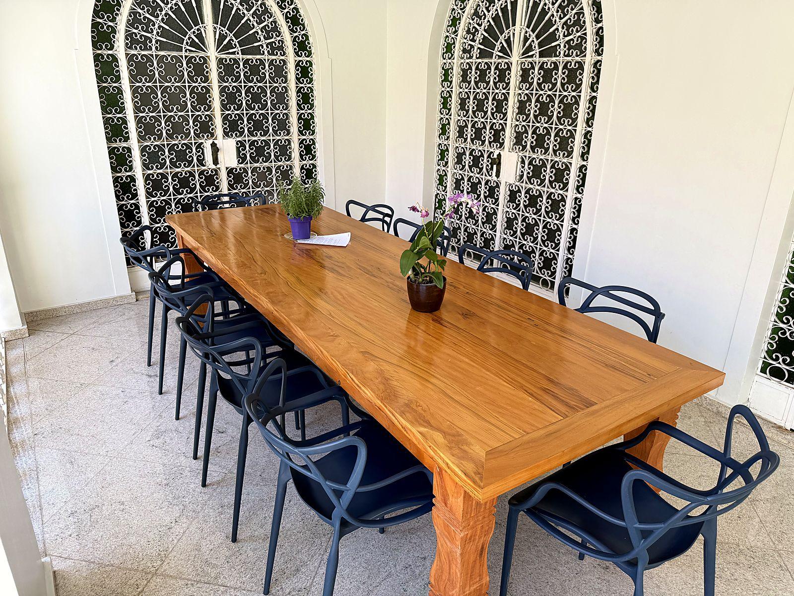 Mesa de madeira para doze pessoas na varanda, diante das portas em arco, pronta para reunião ou almoço