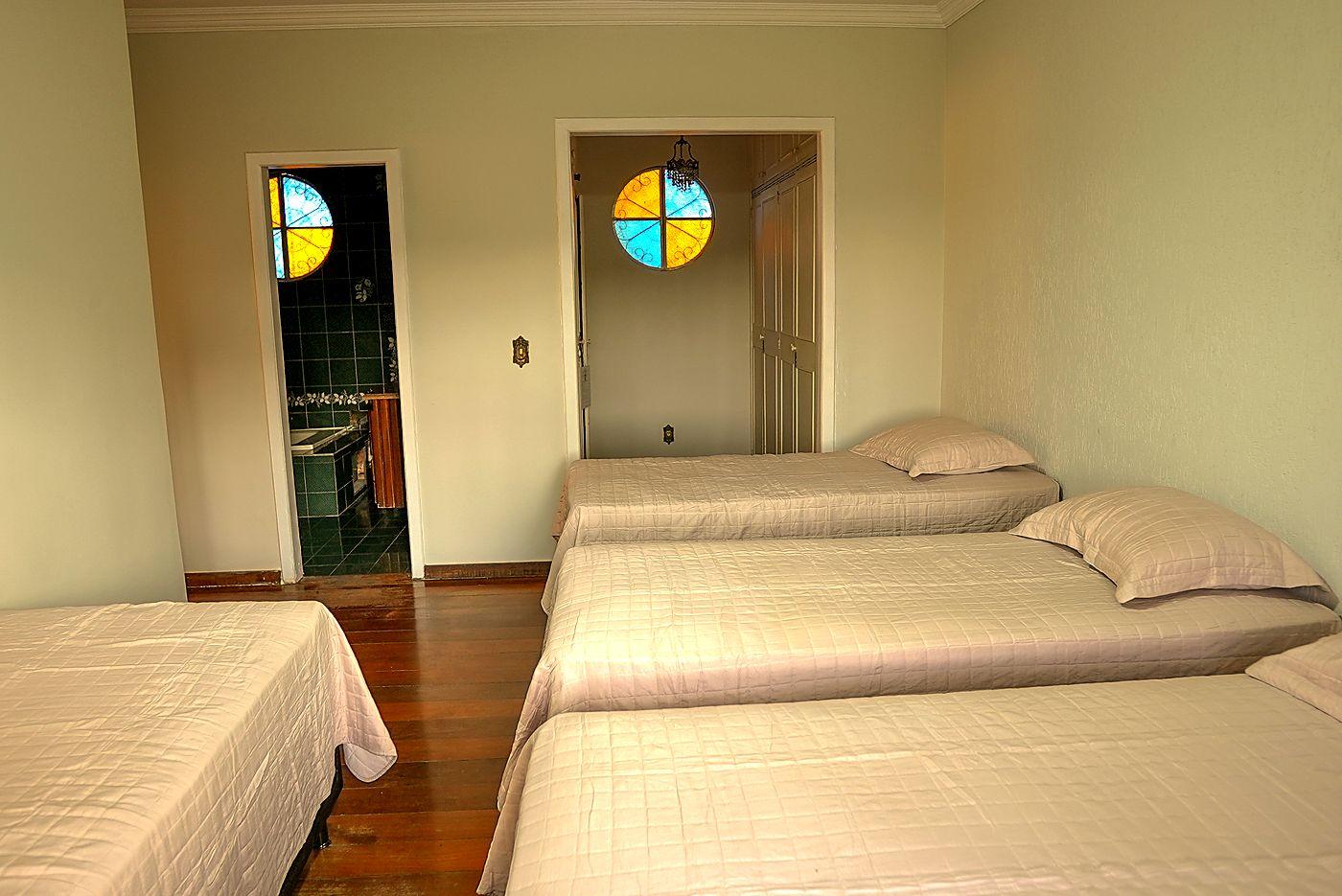 Quarto amplo do Casarão com camas de solteiro, piso de madeira e vitral colorido