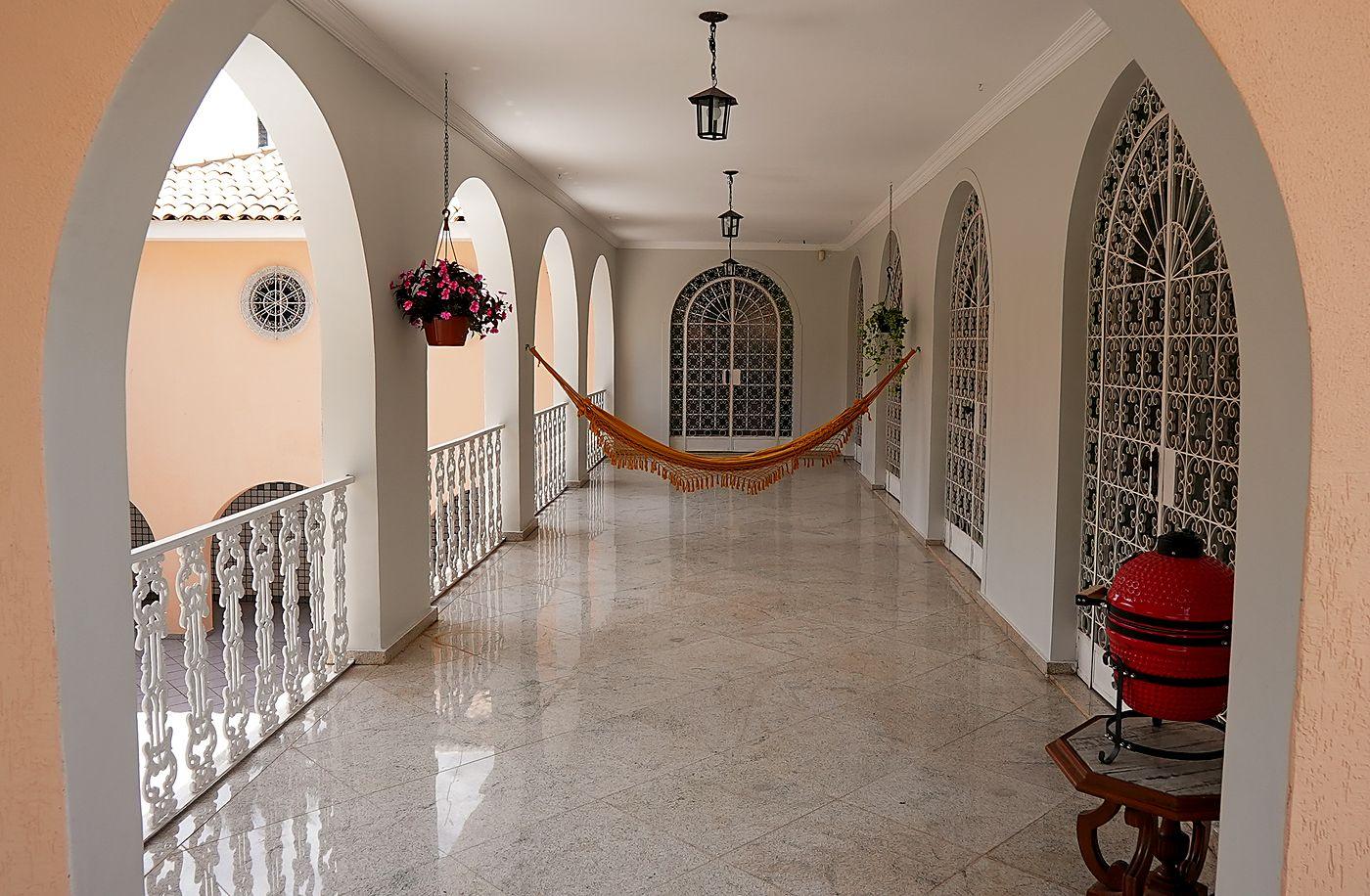 Varanda em arcadas com rede, piso claro e portas em arco